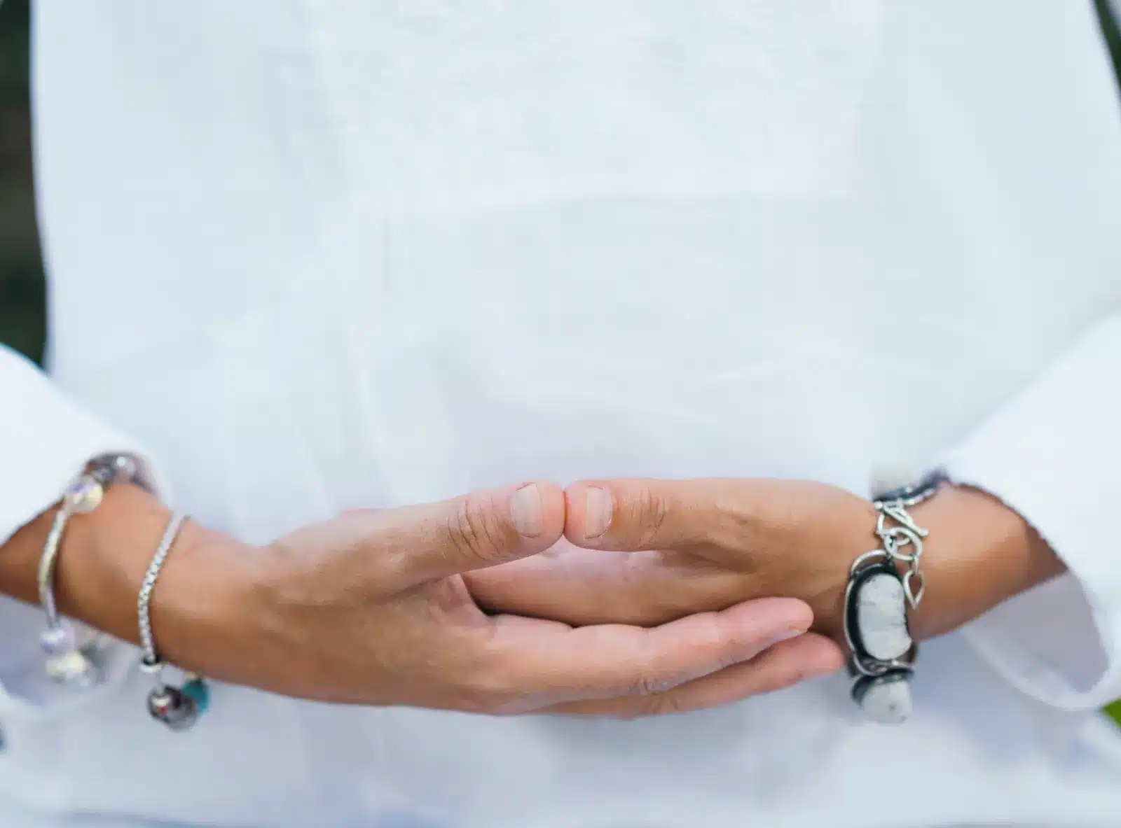 A woman in white meditating outdoors, hands held in a calm gesture